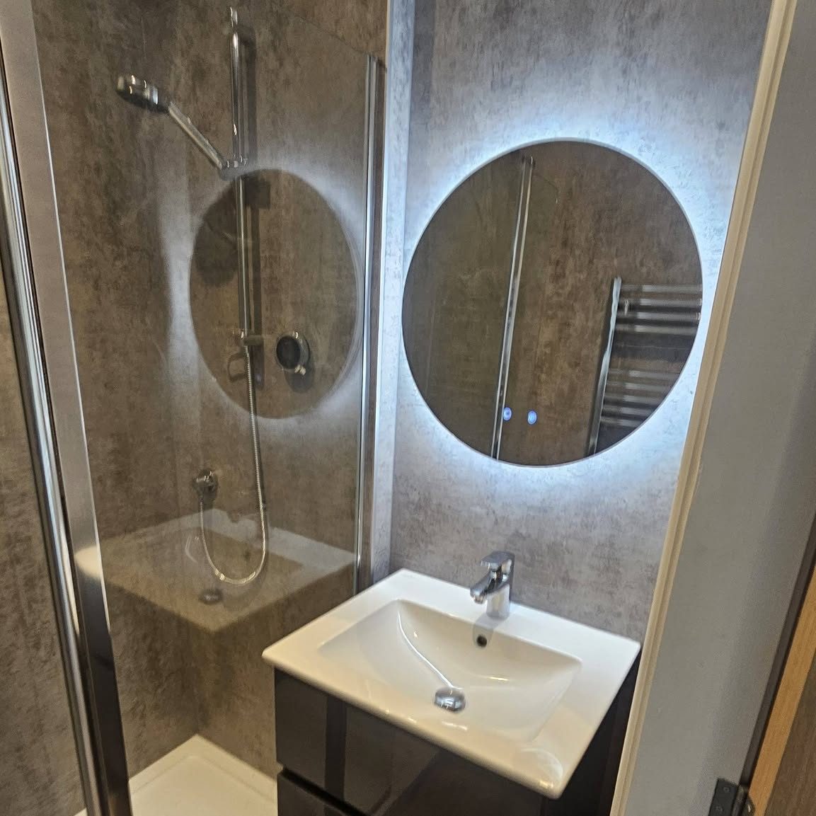 A completed en-suite by Leaghs: backlit round mirror, countertop basin and a quadrant shower